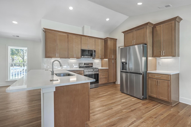 kitchen with appliances with stainless steel finishes, brown cabinetry, light countertops, and a sink