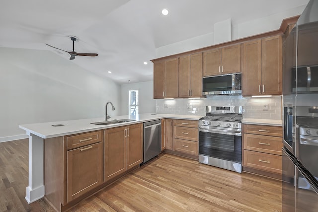 kitchen featuring stainless steel appliances, light countertops, brown cabinetry, a sink, and a peninsula