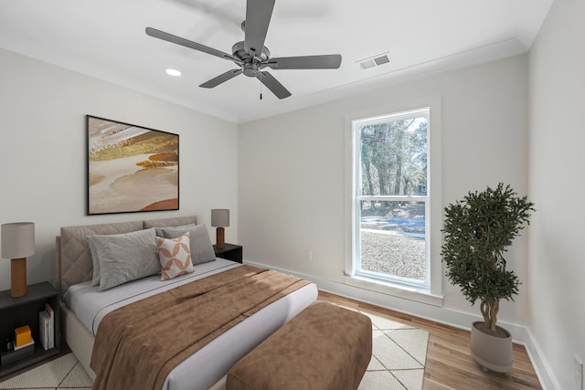 bedroom with crown molding, visible vents, light wood-style flooring, a ceiling fan, and baseboards