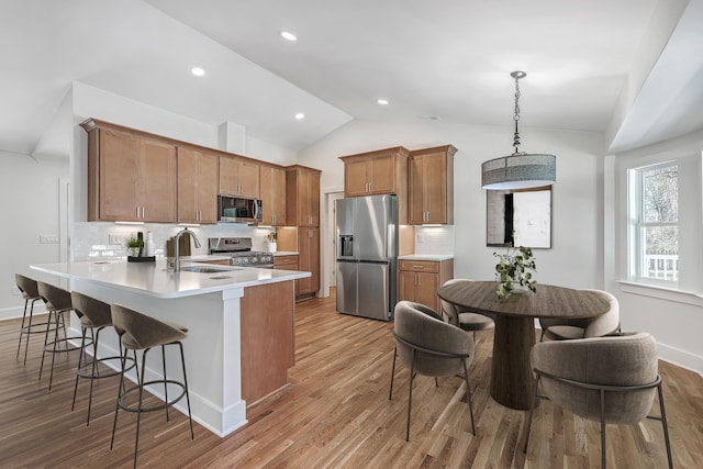 kitchen featuring brown cabinetry, appliances with stainless steel finishes, decorative light fixtures, light countertops, and a sink