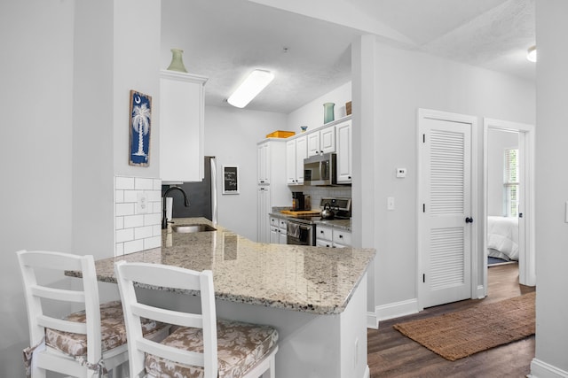 kitchen with dark hardwood / wood-style floors, kitchen peninsula, stainless steel appliances, tasteful backsplash, and sink