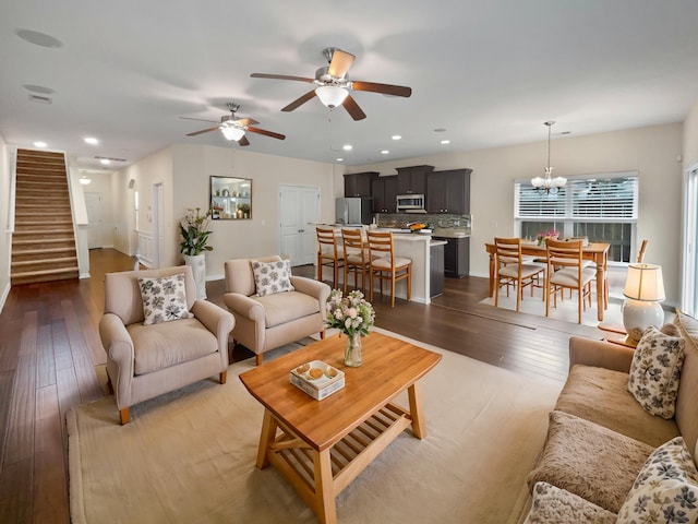 living room with ceiling fan with notable chandelier and dark wood-type flooring