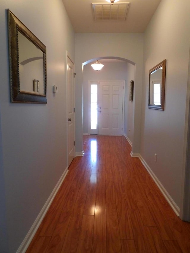 doorway to outside with a wealth of natural light, visible vents, arched walkways, and wood finished floors