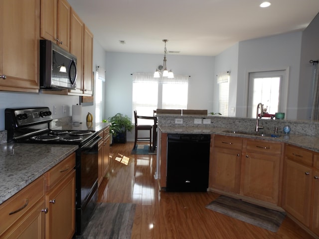 kitchen with light stone countertops, a sink, black appliances, and wood finished floors