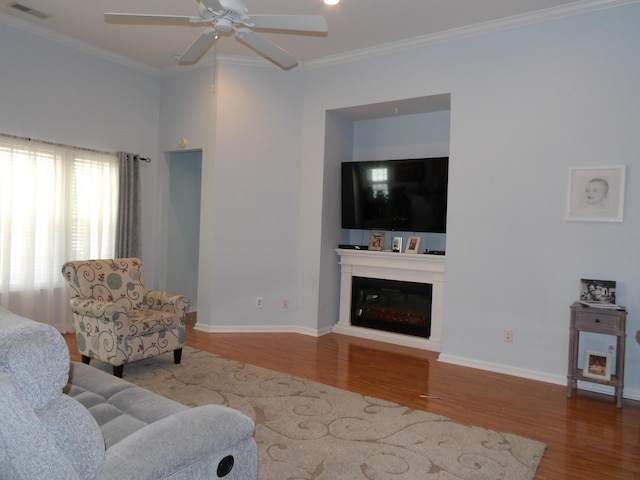 living area with a glass covered fireplace, ornamental molding, wood finished floors, and visible vents