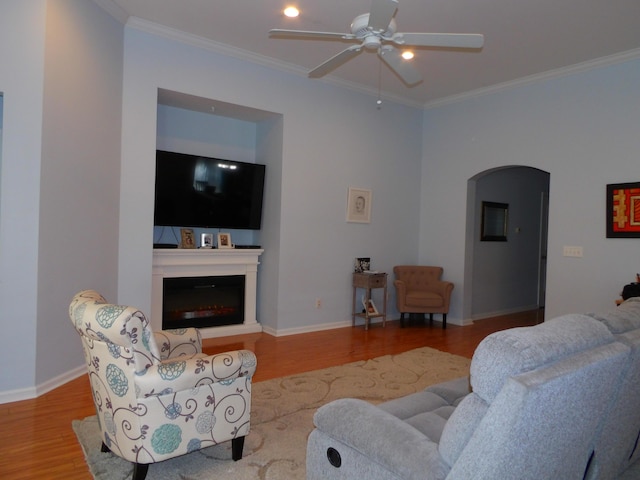 living room featuring crown molding, arched walkways, wood finished floors, and a glass covered fireplace