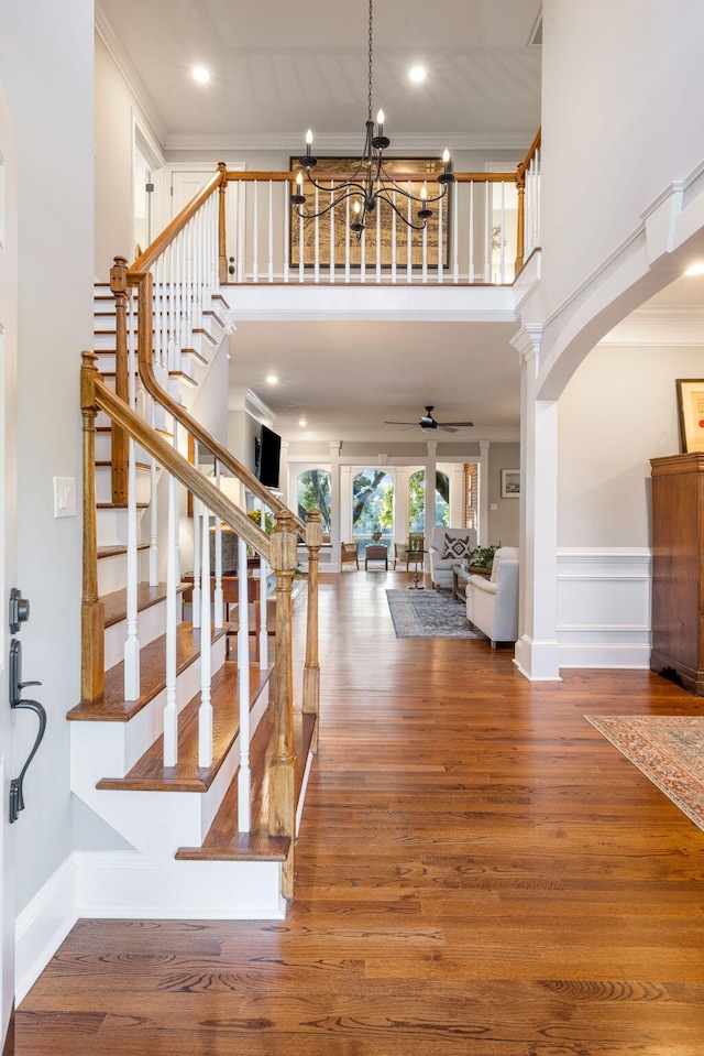 entryway with crown molding, hardwood / wood-style flooring, a high ceiling, decorative columns, and ceiling fan with notable chandelier