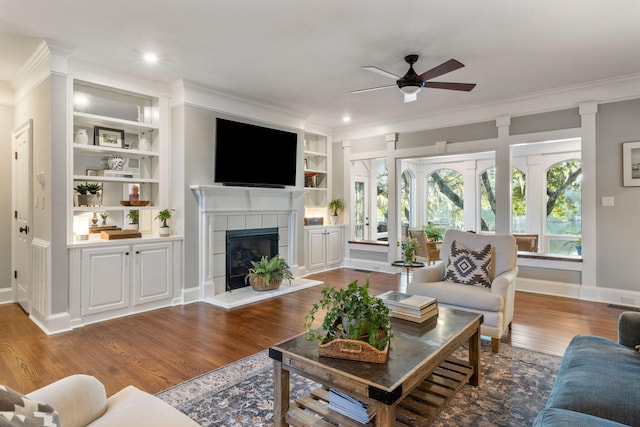 living room featuring built in shelves, a tiled fireplace, hardwood / wood-style floors, and ornamental molding