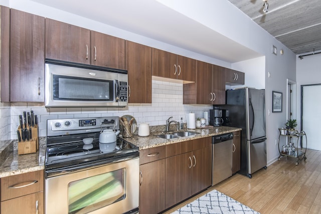 kitchen featuring light hardwood / wood-style flooring, stainless steel appliances, tasteful backsplash, stone counters, and sink