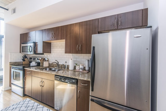 kitchen featuring stainless steel appliances, light wood-type flooring, backsplash, and dark stone counters