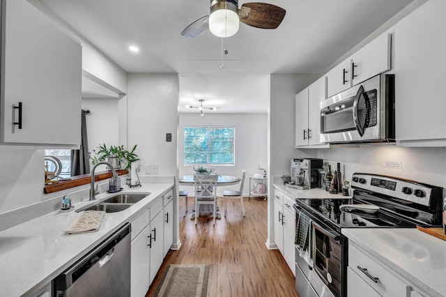 kitchen featuring light wood finished floors, stainless steel appliances, white cabinetry, a sink, and ceiling fan