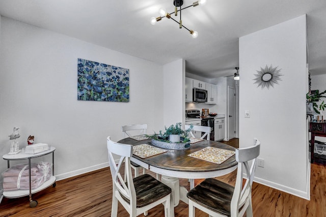 dining space featuring ceiling fan with notable chandelier, wood finished floors, and baseboards