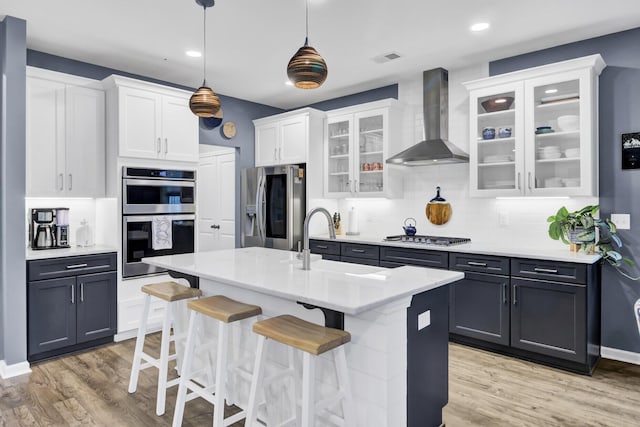 kitchen with pendant lighting, white cabinets, a kitchen breakfast bar, wall chimney exhaust hood, and appliances with stainless steel finishes