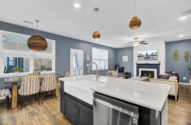 kitchen with light wood-type flooring, stainless steel dishwasher, ceiling fan, sink, and pendant lighting