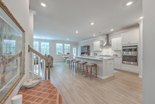 kitchen featuring a kitchen breakfast bar, white cabinets, a center island with sink, decorative backsplash, and wall chimney exhaust hood