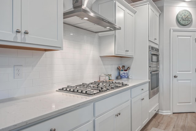 kitchen featuring white cabinetry, light stone counters, stainless steel appliances, decorative backsplash, and exhaust hood