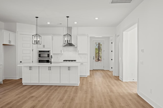 kitchen with white cabinets, wall chimney exhaust hood, black stovetop, light countertops, and double oven