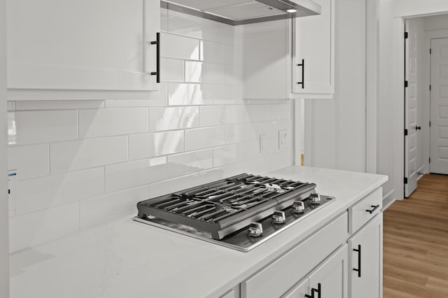 kitchen with tasteful backsplash, white cabinets, light wood-style flooring, stainless steel gas cooktop, and exhaust hood