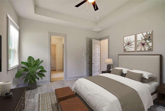 bedroom featuring a raised ceiling, ensuite bathroom, baseboards, and wood finished floors