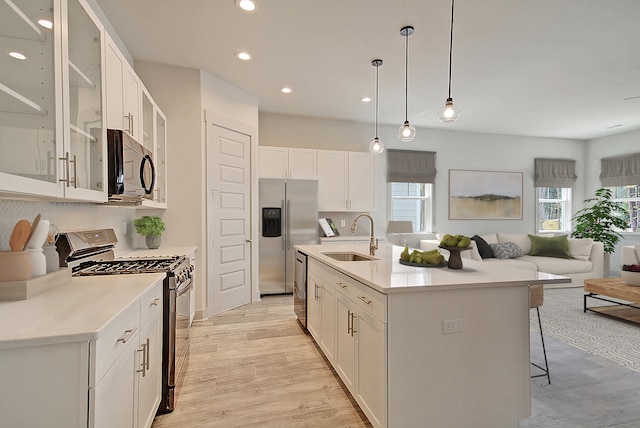 kitchen with a breakfast bar area, open floor plan, stainless steel appliances, light wood-style floors, and a sink