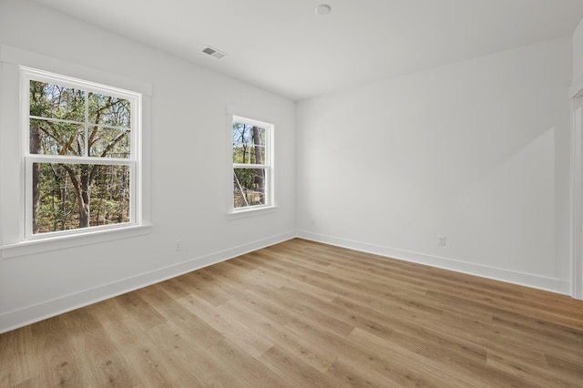 empty room with light wood-type flooring, visible vents, and baseboards