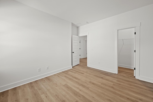 unfurnished bedroom featuring light wood-style floors, a closet, a spacious closet, and baseboards