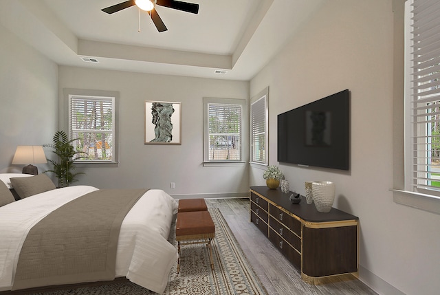 bedroom featuring baseboards, visible vents, a tray ceiling, and wood finished floors