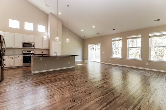 kitchen with dark countertops, appliances with stainless steel finishes, a sink, high vaulted ceiling, and open floor plan