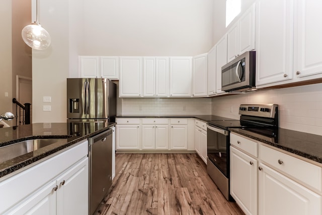 kitchen with backsplash, stainless steel appliances, white cabinetry, and light wood-style flooring