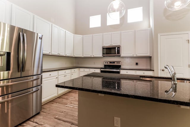kitchen with backsplash, a towering ceiling, appliances with stainless steel finishes, a sink, and white cabinetry