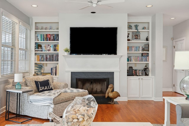 living room with wood-type flooring, built in features, and ceiling fan