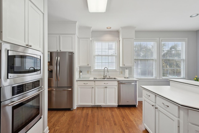 kitchen with appliances with stainless steel finishes, sink, white cabinets, and light wood-type flooring