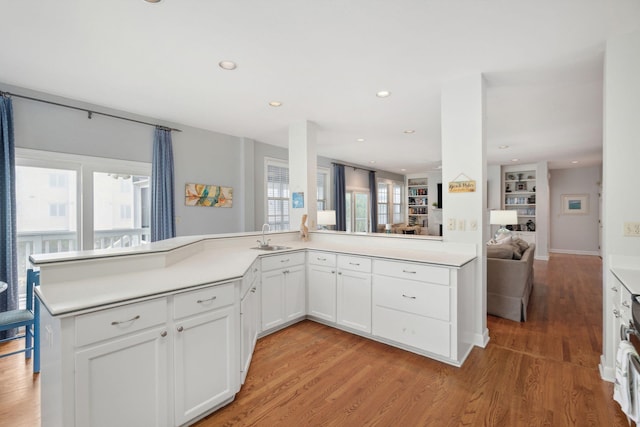 kitchen featuring sink, white cabinetry, light hardwood / wood-style floors, built in shelves, and kitchen peninsula