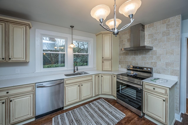 kitchen featuring sink, appliances with stainless steel finishes, hanging light fixtures, cream cabinets, and wall chimney exhaust hood