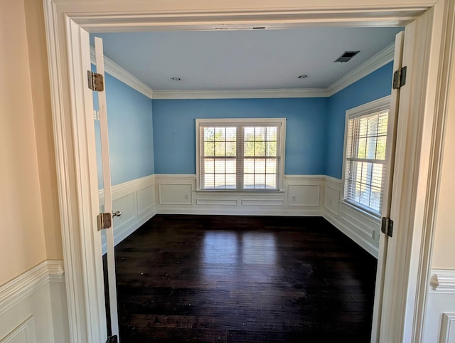 empty room with visible vents, a wainscoted wall, dark wood-type flooring, and ornamental molding