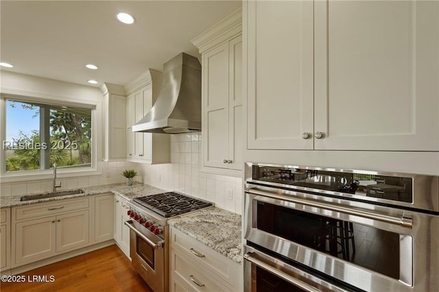 kitchen featuring a sink, stainless steel appliances, wall chimney range hood, backsplash, and recessed lighting