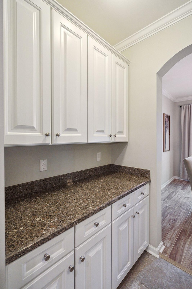 kitchen with white cabinetry, ornamental molding, and dark stone countertops