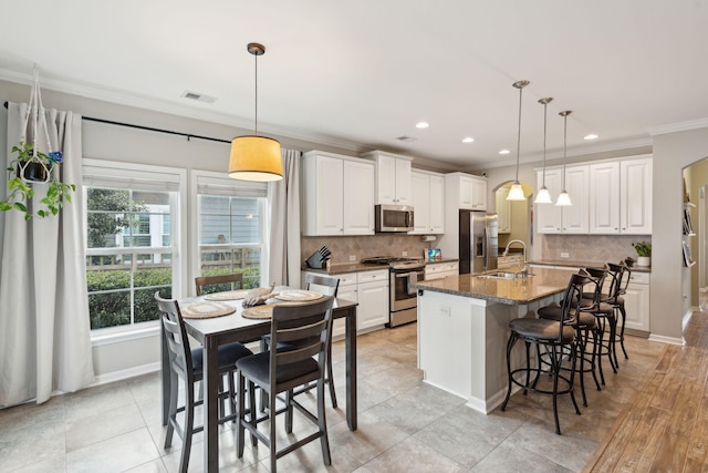 kitchen with appliances with stainless steel finishes, a kitchen island with sink, sink, and pendant lighting