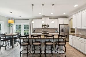 kitchen featuring appliances with stainless steel finishes, a kitchen island with sink, hanging light fixtures, tasteful backsplash, and white cabinets