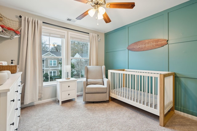 carpeted bedroom featuring a nursery area, ceiling fan, and multiple windows