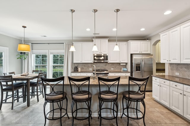 kitchen with white cabinetry, a center island with sink, dark stone counters, pendant lighting, and stainless steel appliances