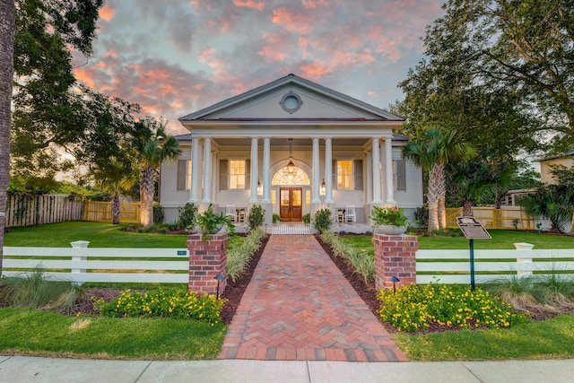 greek revival house with a yard, fence, and covered porch