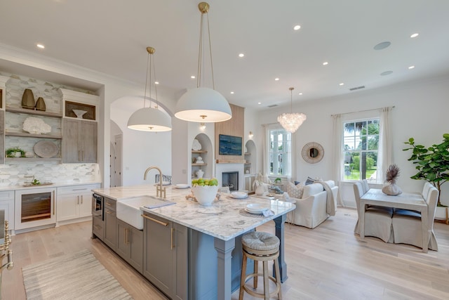 kitchen with gray cabinets, a sink, open shelves, light wood finished floors, and light stone countertops