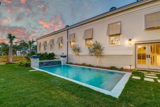 outdoor pool with french doors, a lawn, and fence