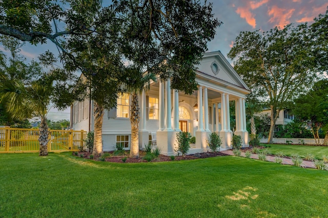 neoclassical home featuring a front yard and fence