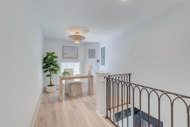 corridor with an upstairs landing, electric panel, light wood-type flooring, and baseboards