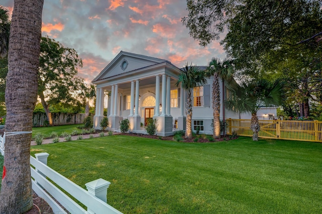 greek revival house featuring covered porch, a front yard, and fence