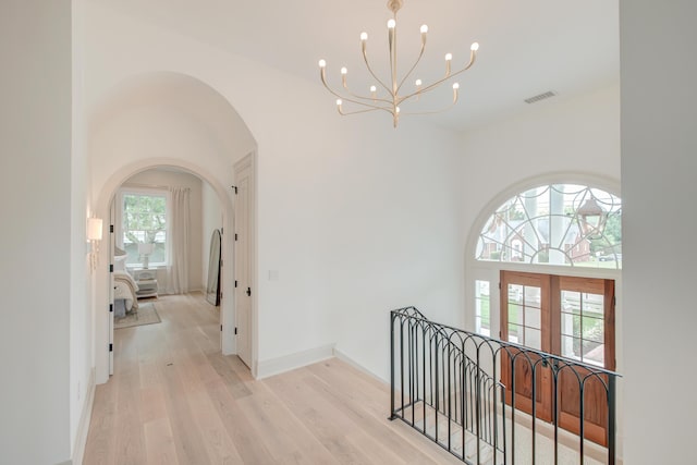 hallway with visible vents, a chandelier, a high ceiling, light wood-style floors, and arched walkways