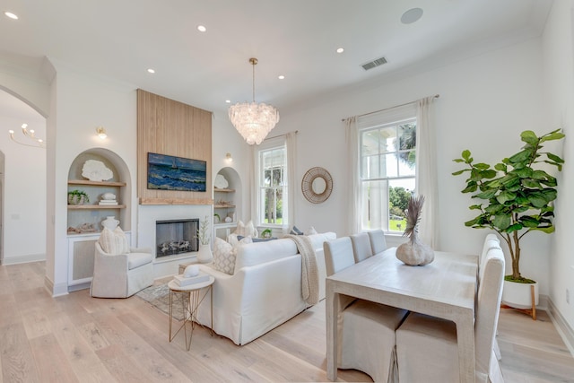 living area with an inviting chandelier, built in features, visible vents, and light wood finished floors