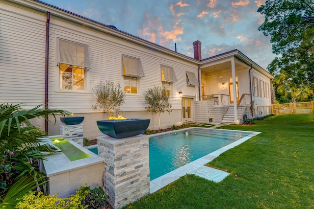 back of house at dusk featuring a yard, a fenced in pool, a chimney, and fence